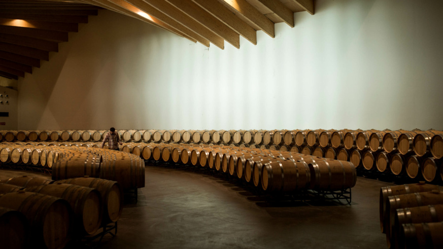 ysios - 100s of wine barrels in a modern looking building with a man inspecting a barrel