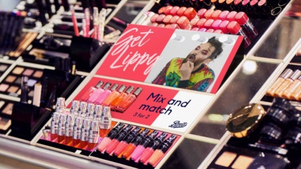Boots - 'Get Lippy' lipstick display with many different colours of lipstick and lipgloss, with a photo of a non-binary model applying lip gloss in the centre.