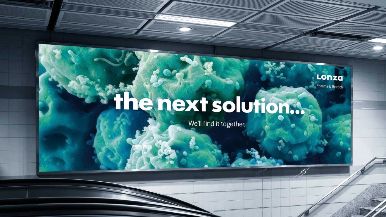 Lonza - a billboard stating 'the next solution... We'll find it together.' with a set of stairs and escalators in the foreground.