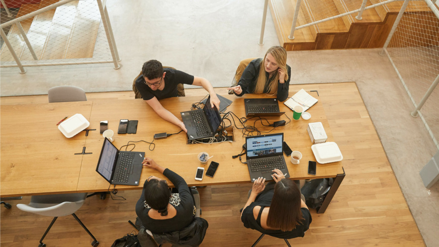 4 People doing work on laptops on a large wooden table