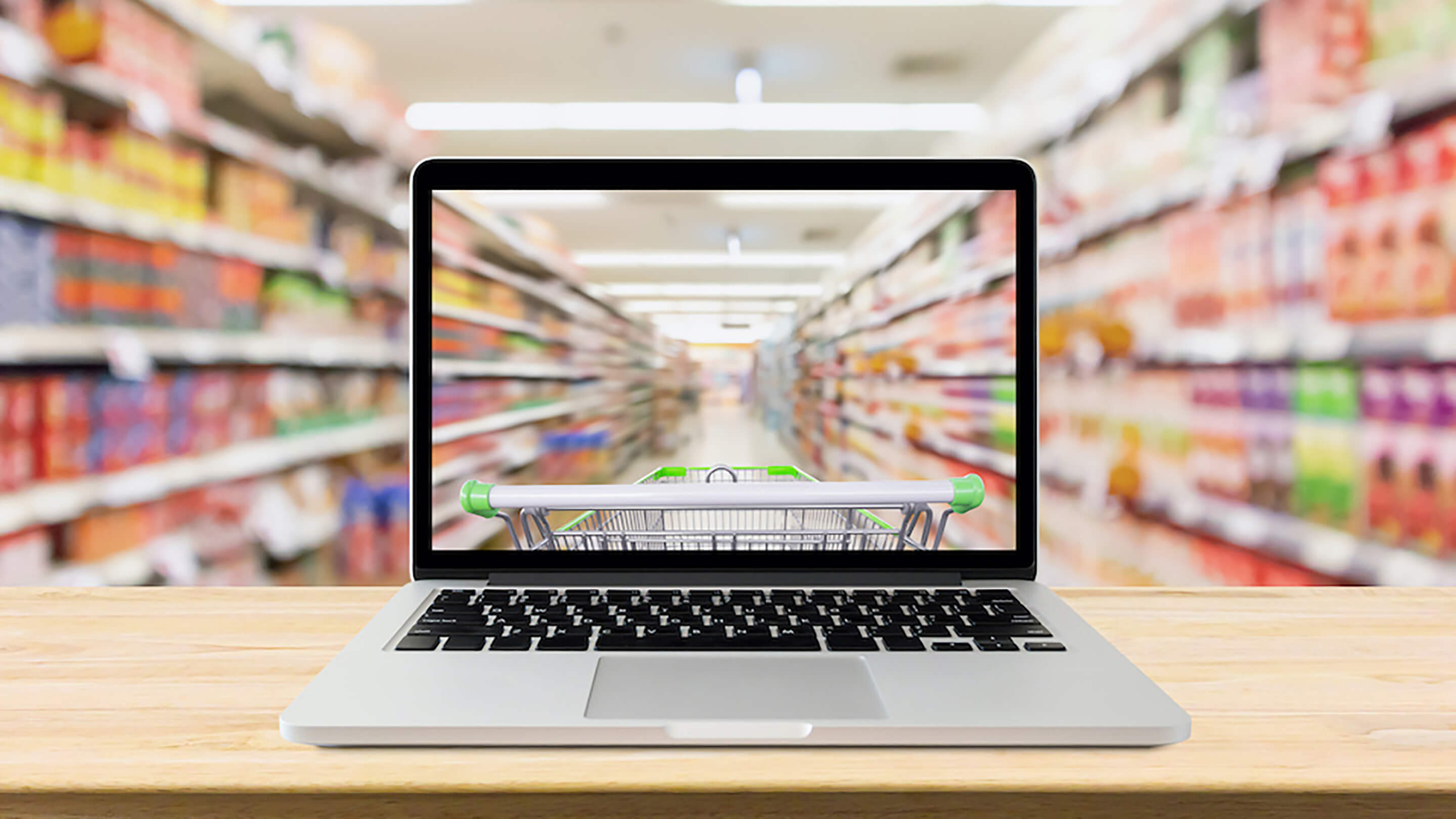 A laptop with a supermarket trolley inside. In the background is actual supermarket aisles