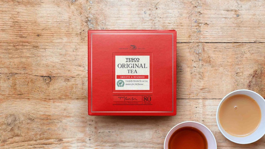"A box of Tesco Original Tea with two cups of brewed tea on a wooden surface."