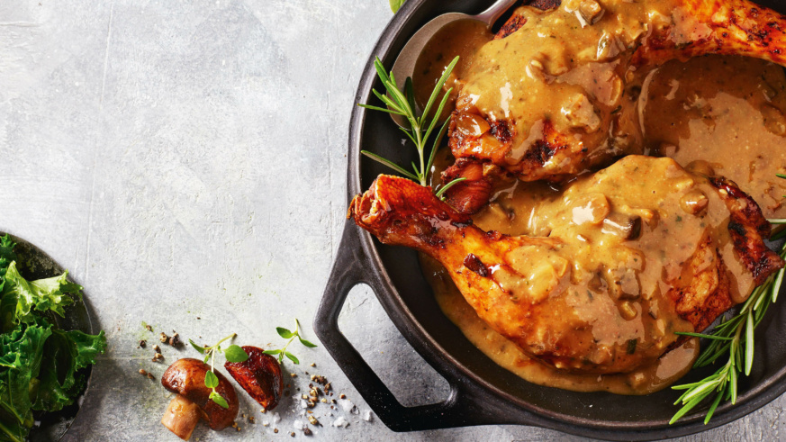 "Roasted chicken legs in a creamy mushroom sauce garnished with rosemary in a black skillet."