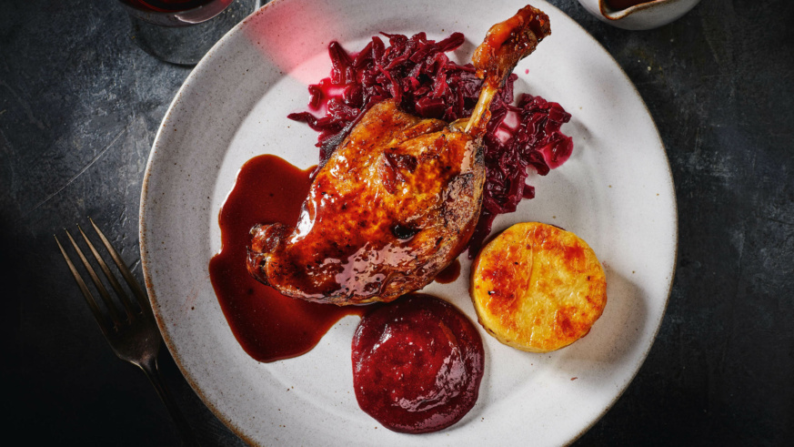 "Duck leg confit with red cabbage, potato gratin, and rich sauce on a white plate."