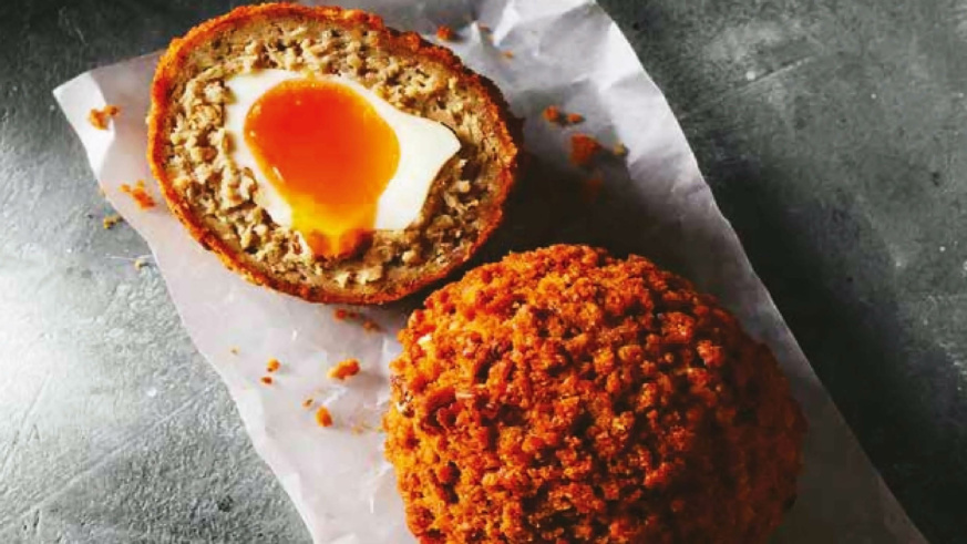 "Halved Scotch egg with a runny yolk, served on parchment paper."