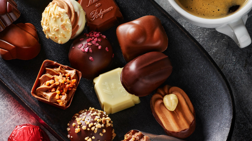 "Assorted Belgian chocolates with various toppings and fillings next to a cup of coffee."