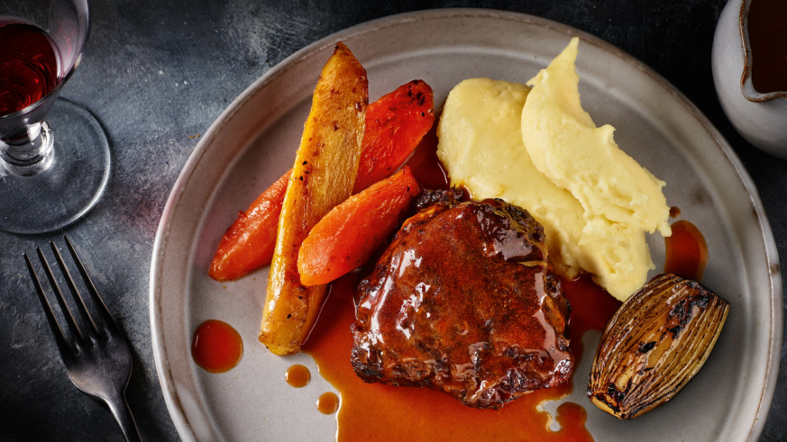"Beef Cheek served with roasted carrots, mashed potatoes, and caramelized shallot, served with a glass of red wine."