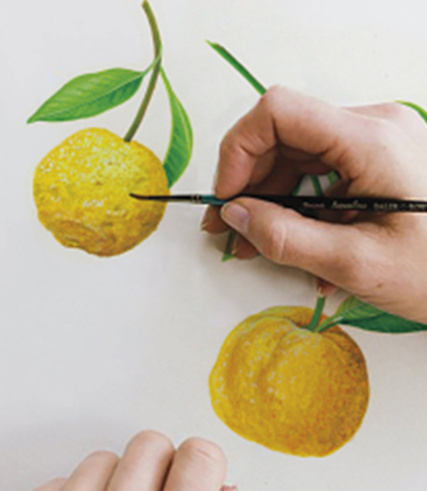 "Close-up of hands painting vibrant yellow citrus fruits with green leaves."