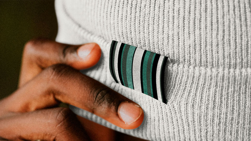 "Martin Guitars beanie detail: Finger pointing to green and black striped logo tag on a light gray knit beanie."