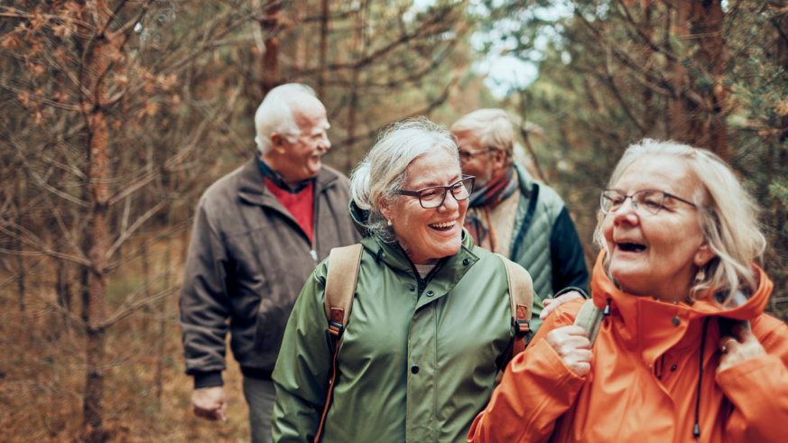 "Group of happy senior friends hiking and laughing in a forest."