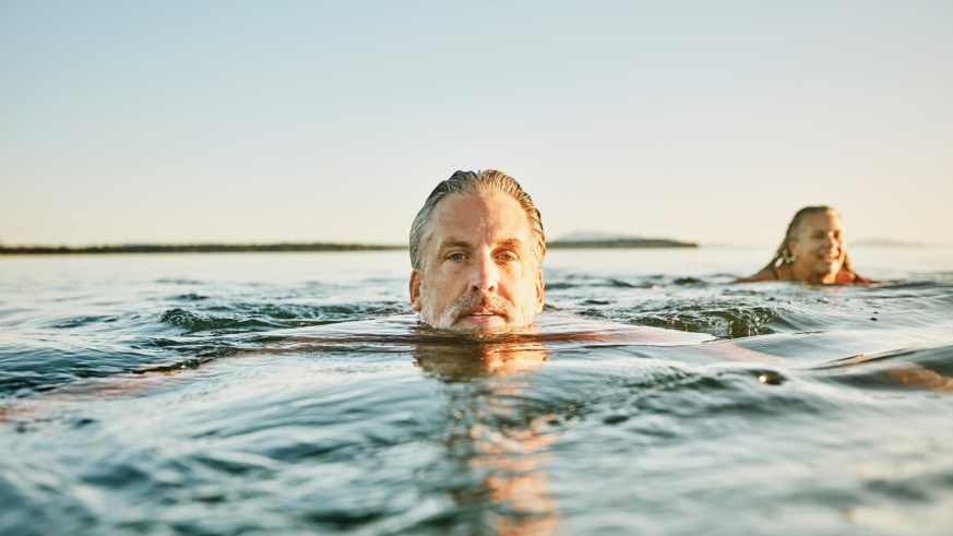 "Mature man swimming in the ocean with a woman in the background."