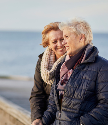 "Two smiling senior women standing by a railing overlooking the ocean."
