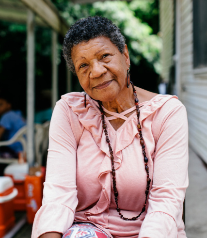 "Portrait of a smiling senior woman wearing a pink shirt and a beaded necklace."