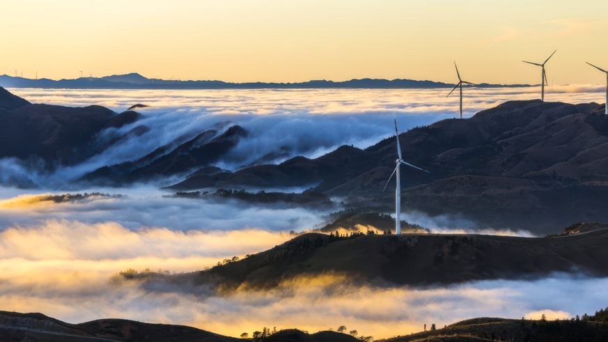 "Example of Cargill's photography princples showing wind turbines standing tall on rolling hills shrouded in clouds, capturing the morning light as the sun rises."